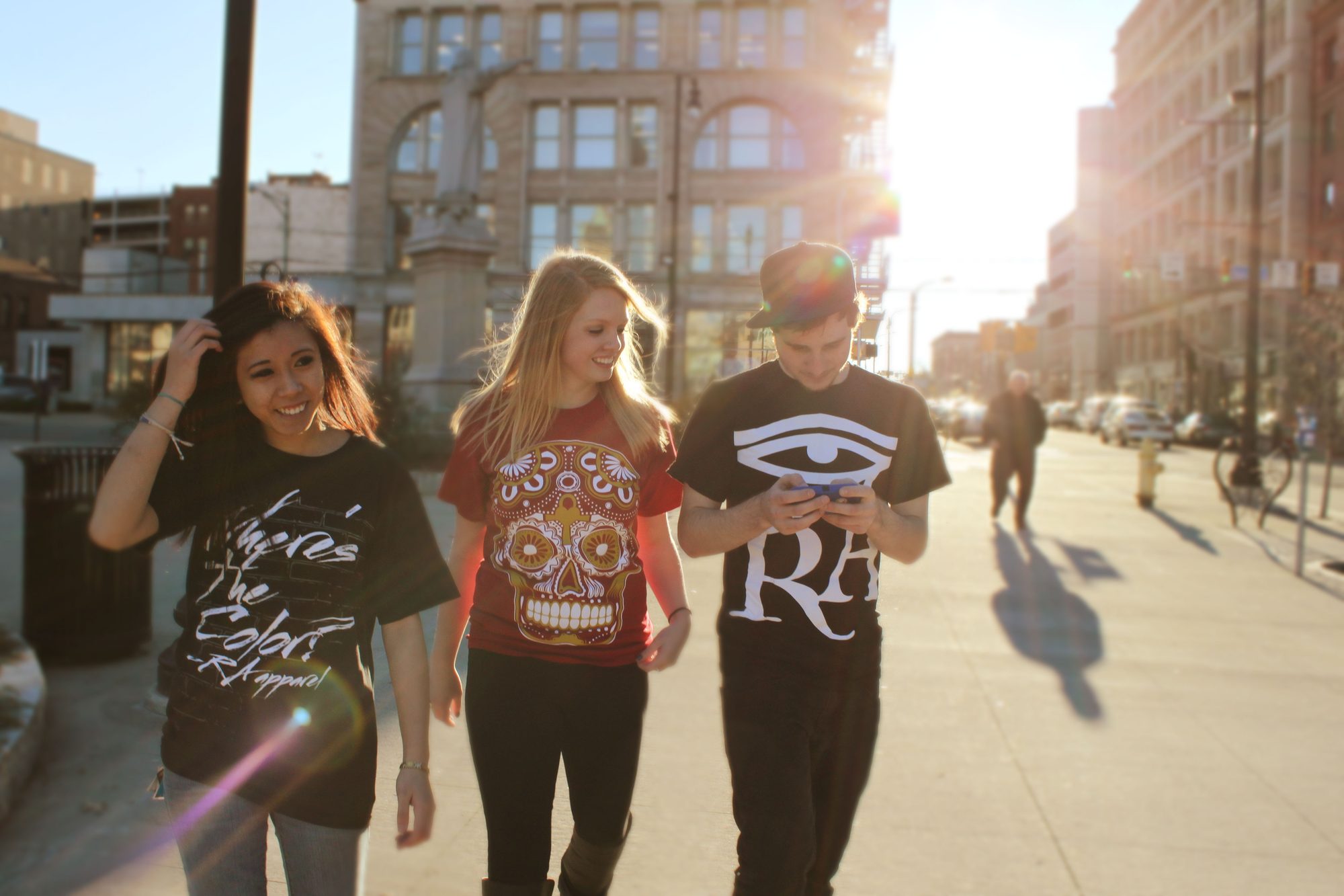 Three people wearing RA Apparel shirts walking on a city sidewalk